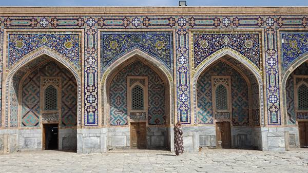 Donna cammina davanti alla facciata maiolicata del Registan a Samarcanda