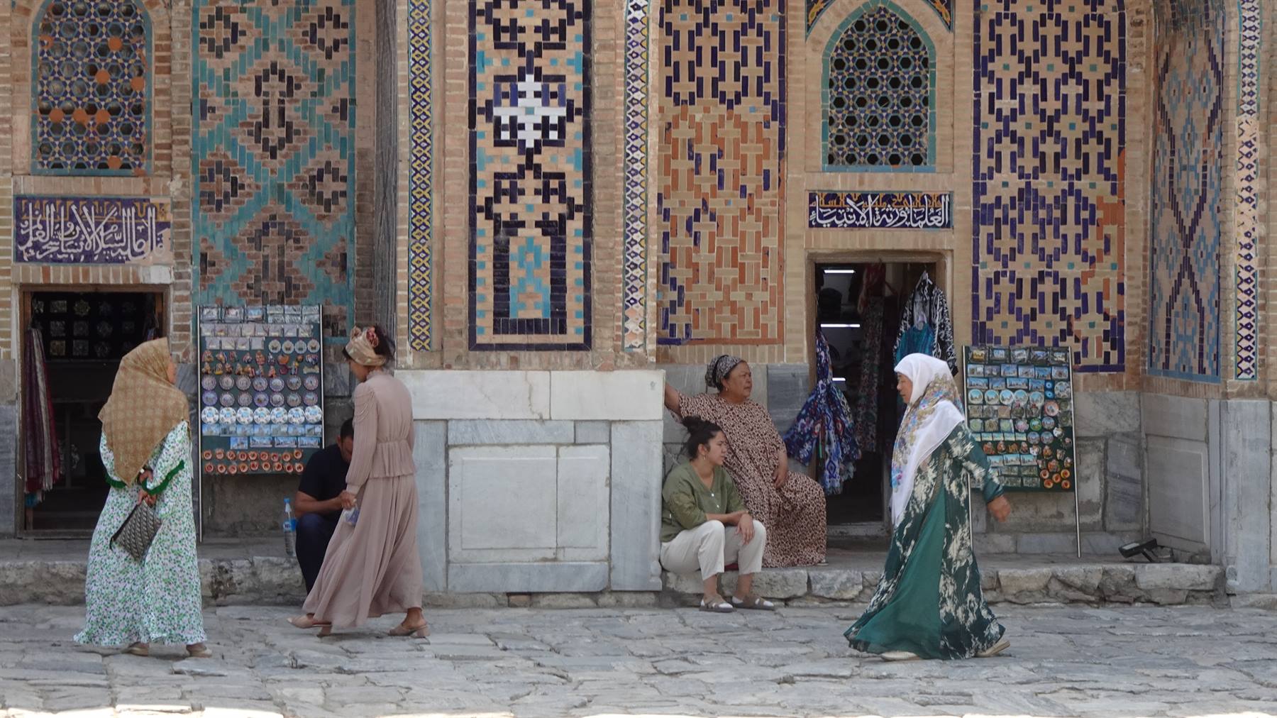 Donne in abiti tradizionali passeggiano davanti alle maioliche del Registan, Samarcanda