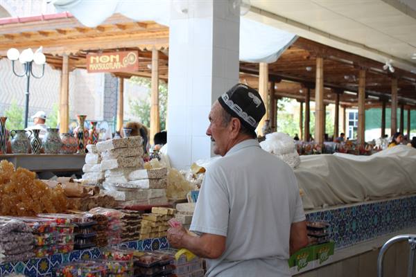 Venditore con doppiok al bazar di Chorsu a Tashkent tra dolci e canditi