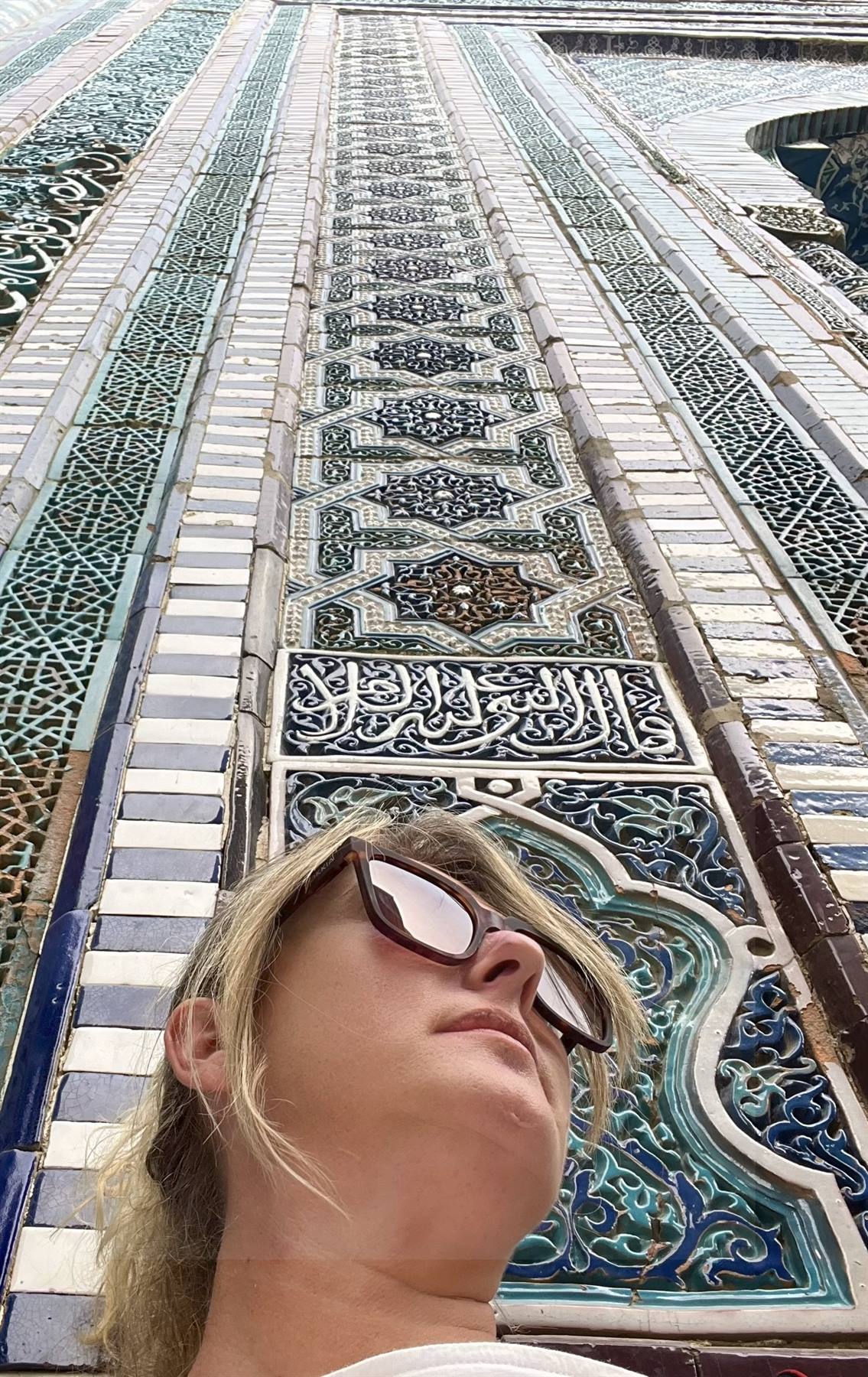 Donna con occhiali scuri sotto mosaici maiolicati a Samarcanda