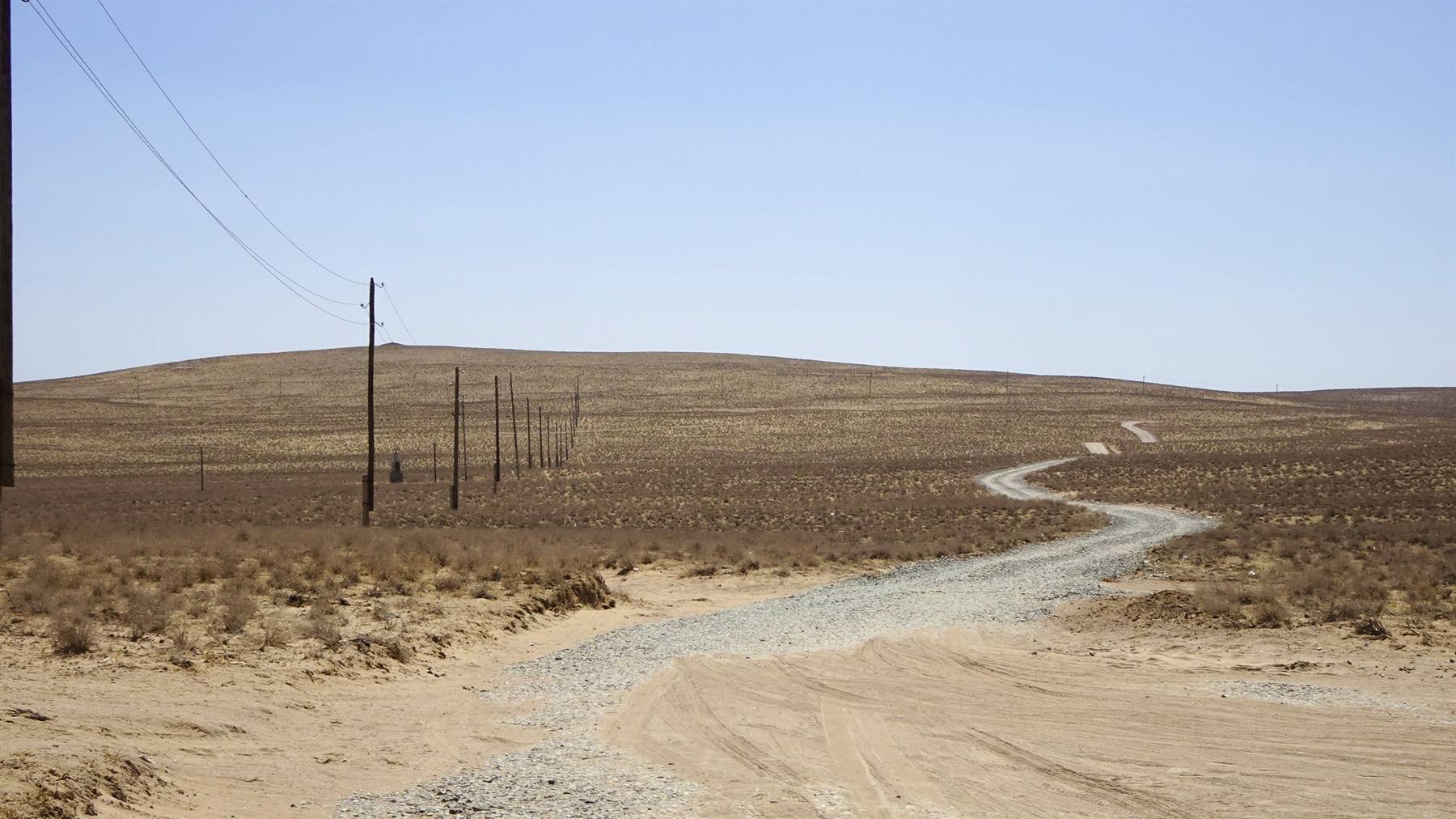 Strada sterrata tra le dune del deserto Kizilkum, piloni electricity… meglio: Pali della luce lungo 