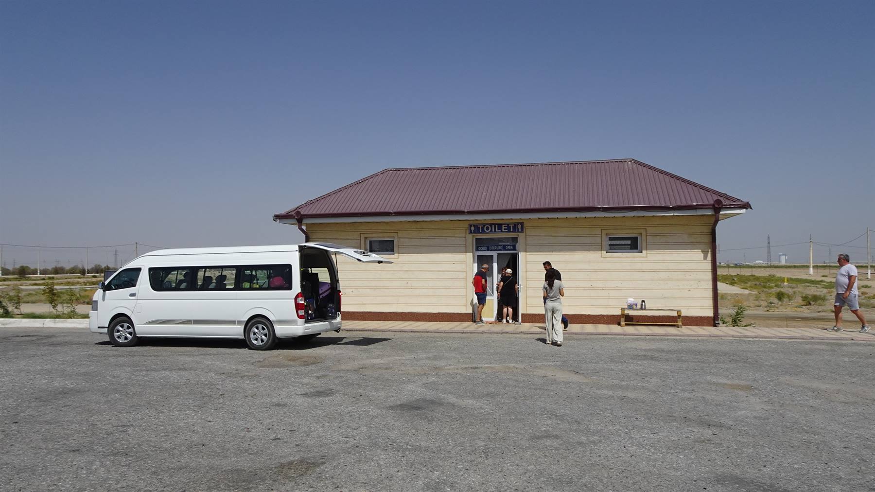 Piccola stazione nel deserto: furgone bianco parcheggiato e passeggeri che aspettano