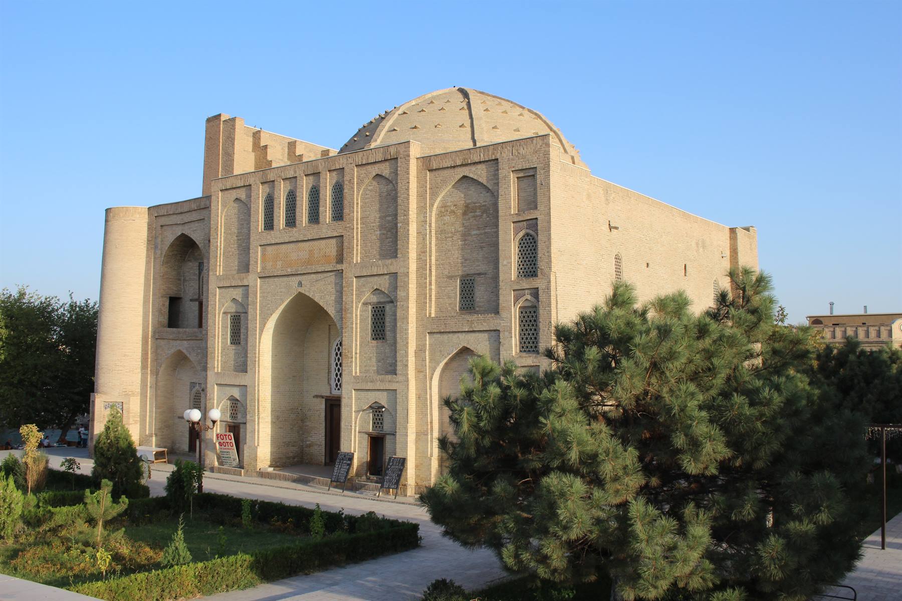 Madrasa in mattoni di sabbia con cupola e portale, tra pini, a Bukhara