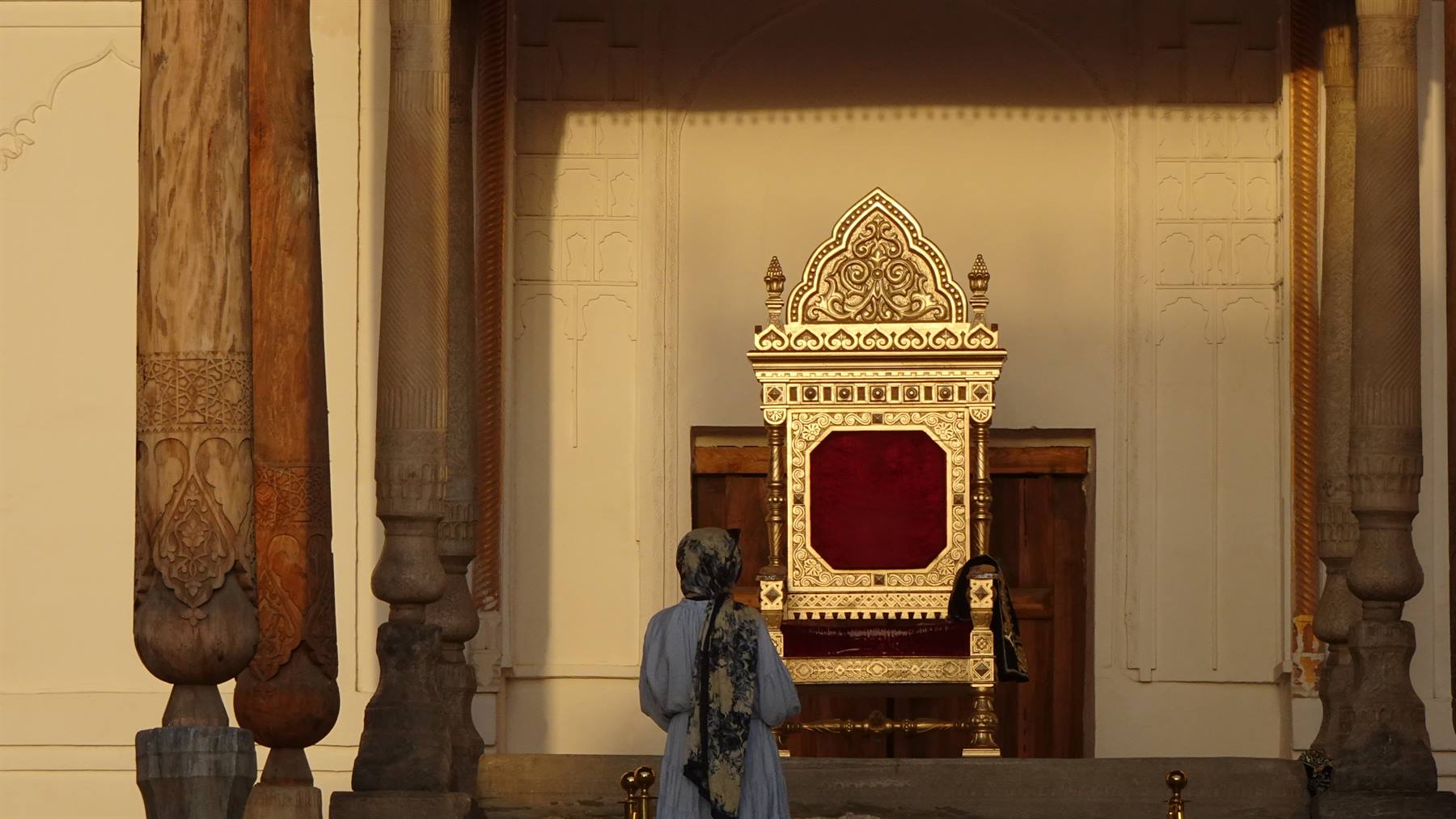 Donna davanti a un trono dorato intarsiato nel palazzo di Bukhara
