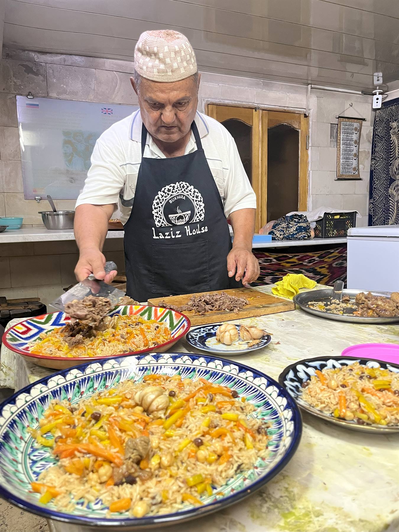 Lo chef mette la carne sul plov nei piatti ceramici decorati, cucina di Tashkent
