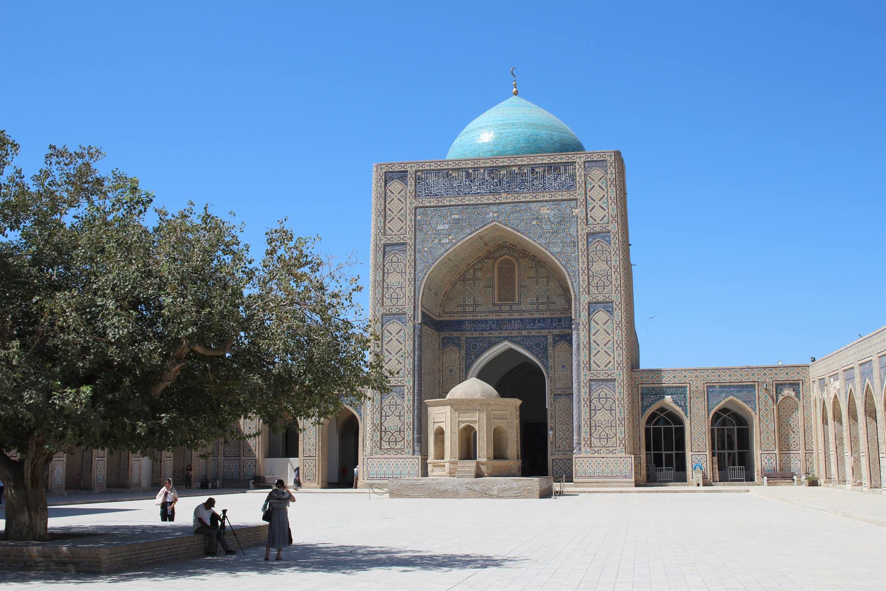 Turisti fotografano il grande iwan a mosaici e la cupola turchese della moschea, Bukhara