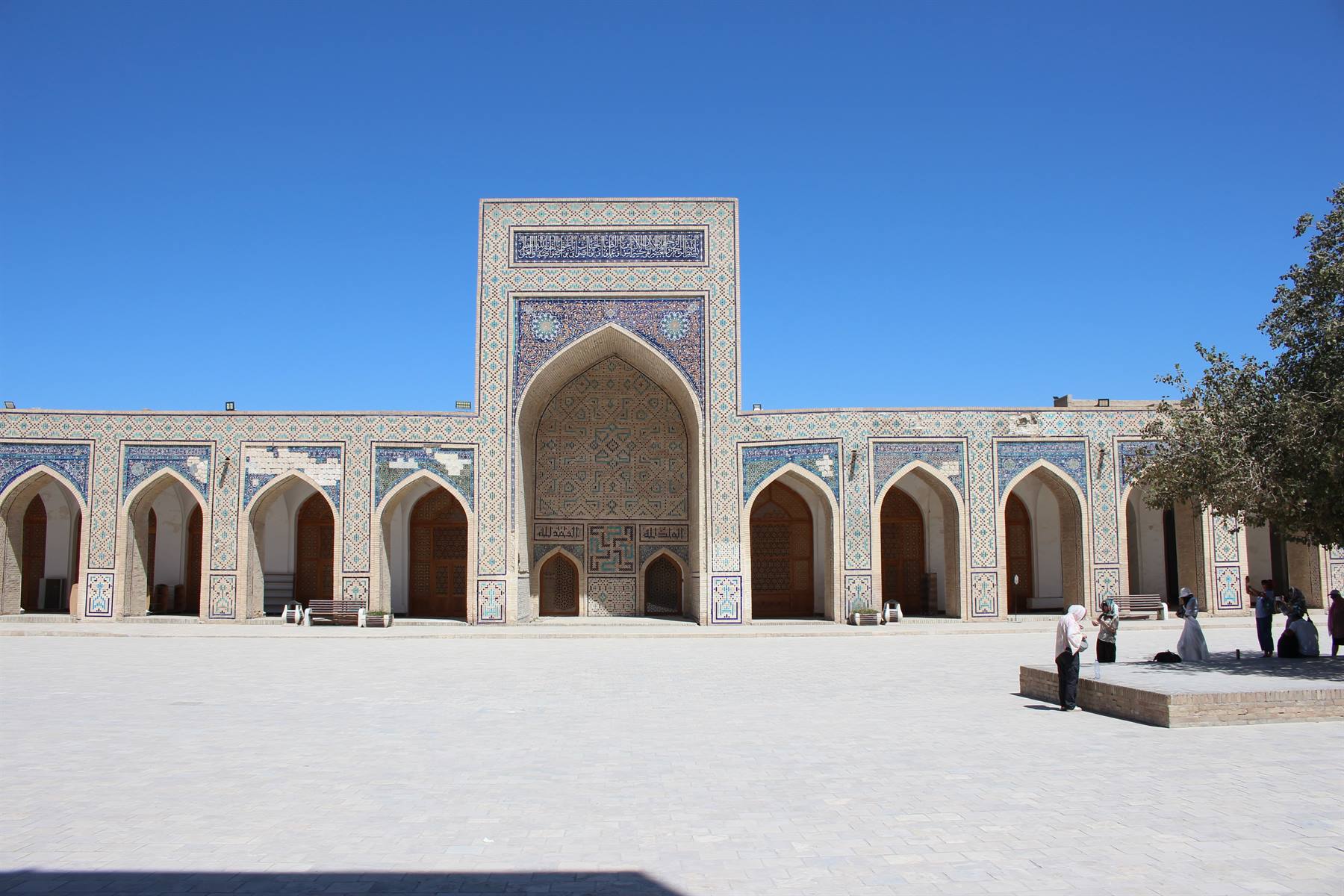 Piazza con medressa di mattoni e maioliche blu, turisti camminano, Bukhara