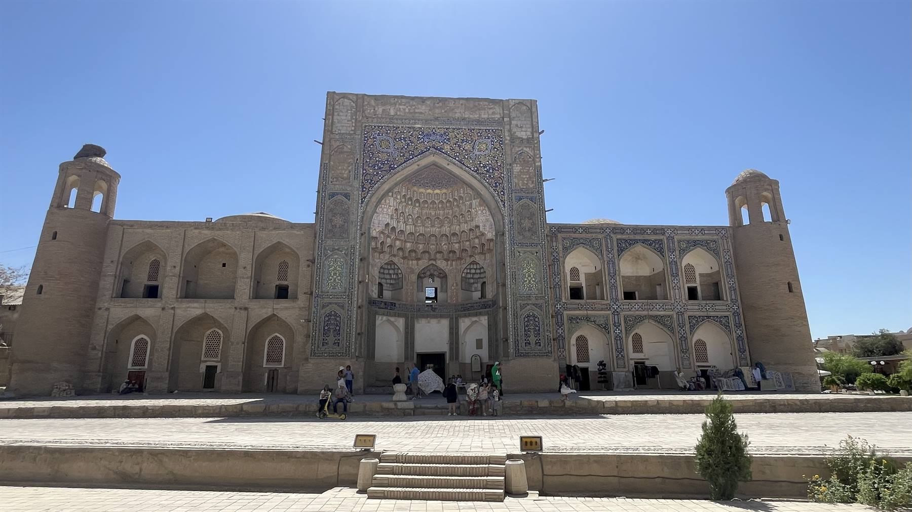 Madrasa in mattoni sabbia con maioliche blu, visitatori sotto il grande portale
