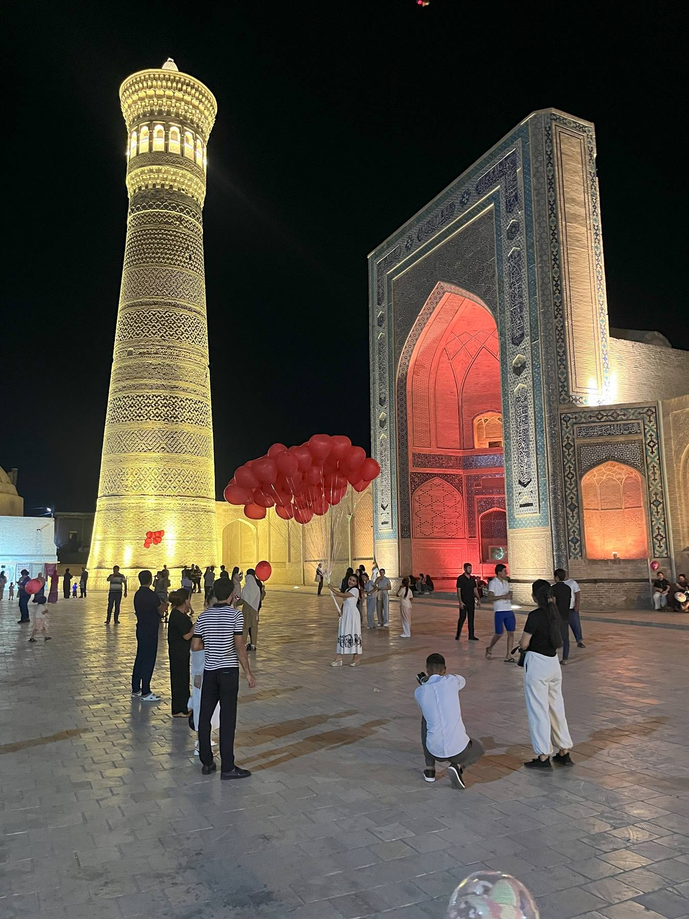 Bukhara, notte: turisti con palloncini rossi accanto al minareto illuminato