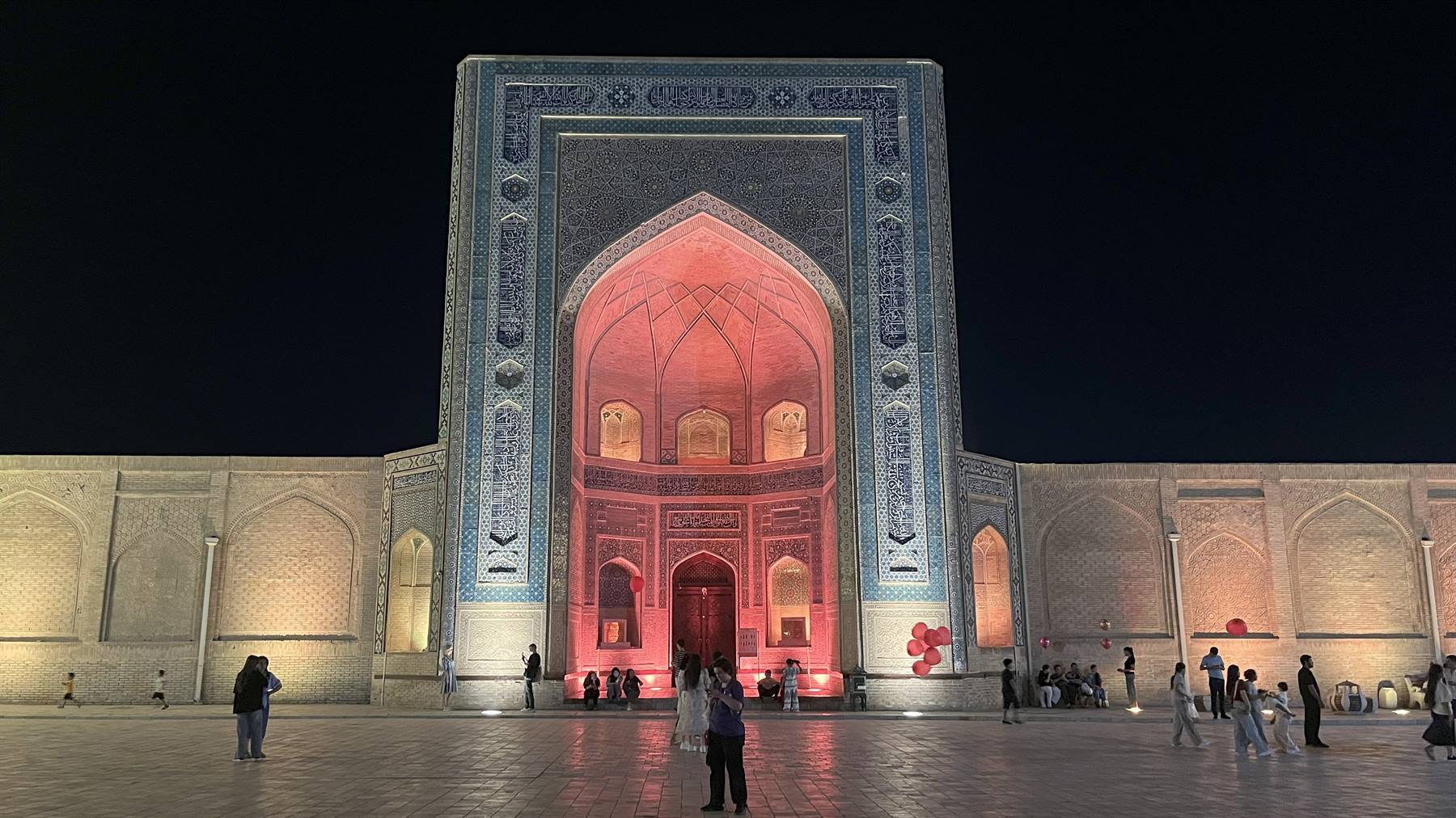 Portale in maiolica blu illuminato di rosso di notte, piazza con visitatori