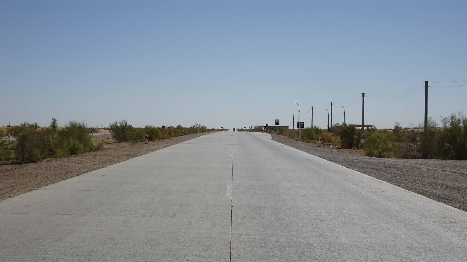 Strada asfaltata dritta tra arbusti secchi e pali elettrici, cielo azzurro