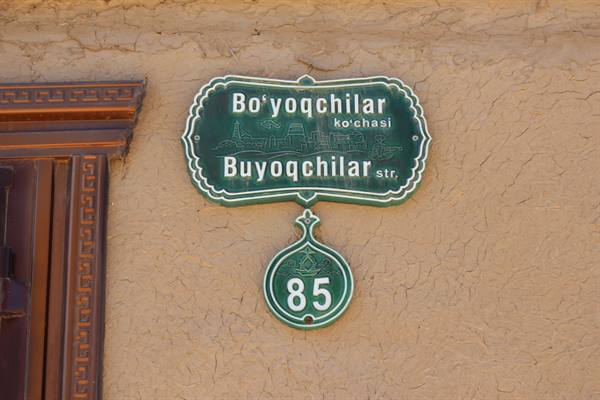 Insegna verde della via Bo'yoqchilar con numero civico 85 su muro crudo