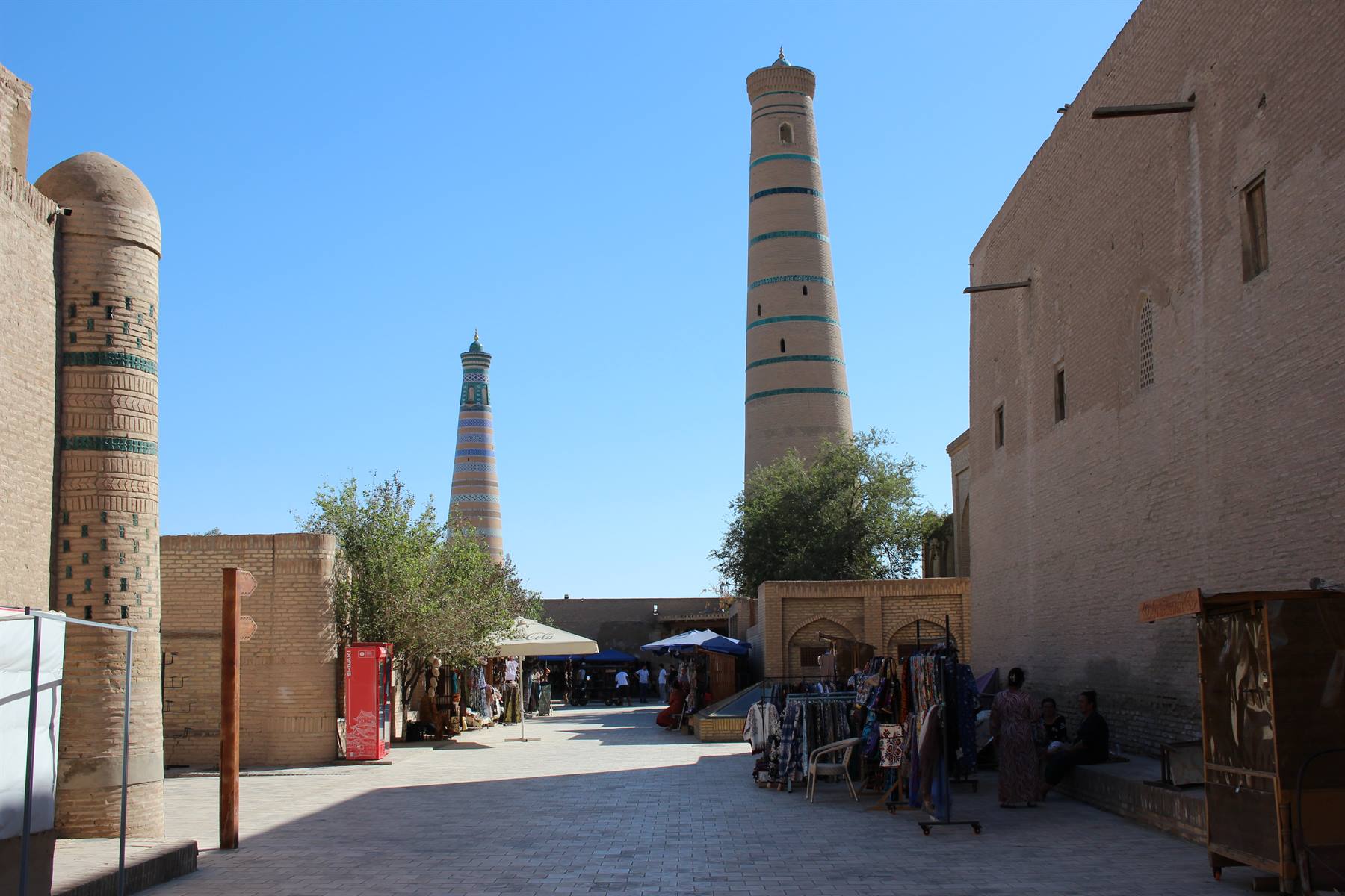 Minareti in mattoni a Khiva, mercatino all'ombra sotto il cielo azzurro
