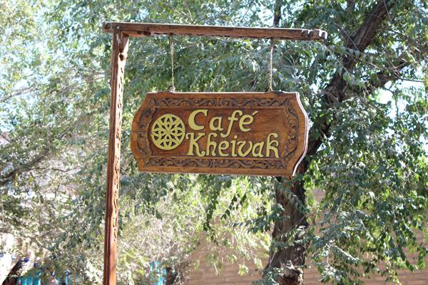 Insegna di legno intagliato del Café Kheivak tra gli alberi di Bukhara