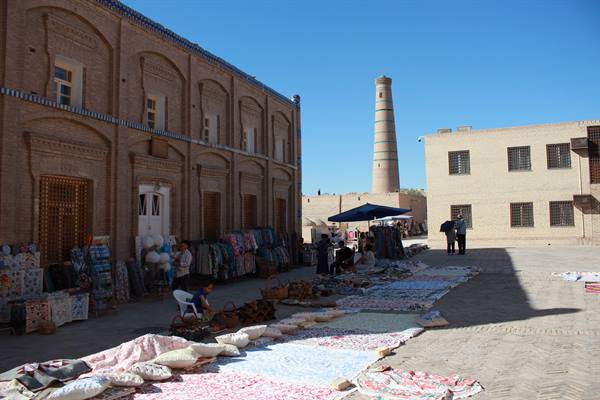 Mercato di tappeti e stoffe davanti ai mattoni antichi, minaretto di Khiva