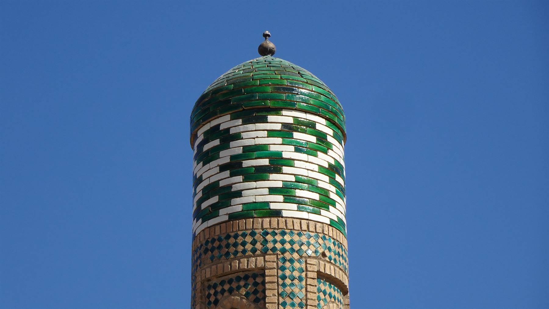Minareto decorato con maioliche verdi e bianche sotto il cielo blu di Khiva