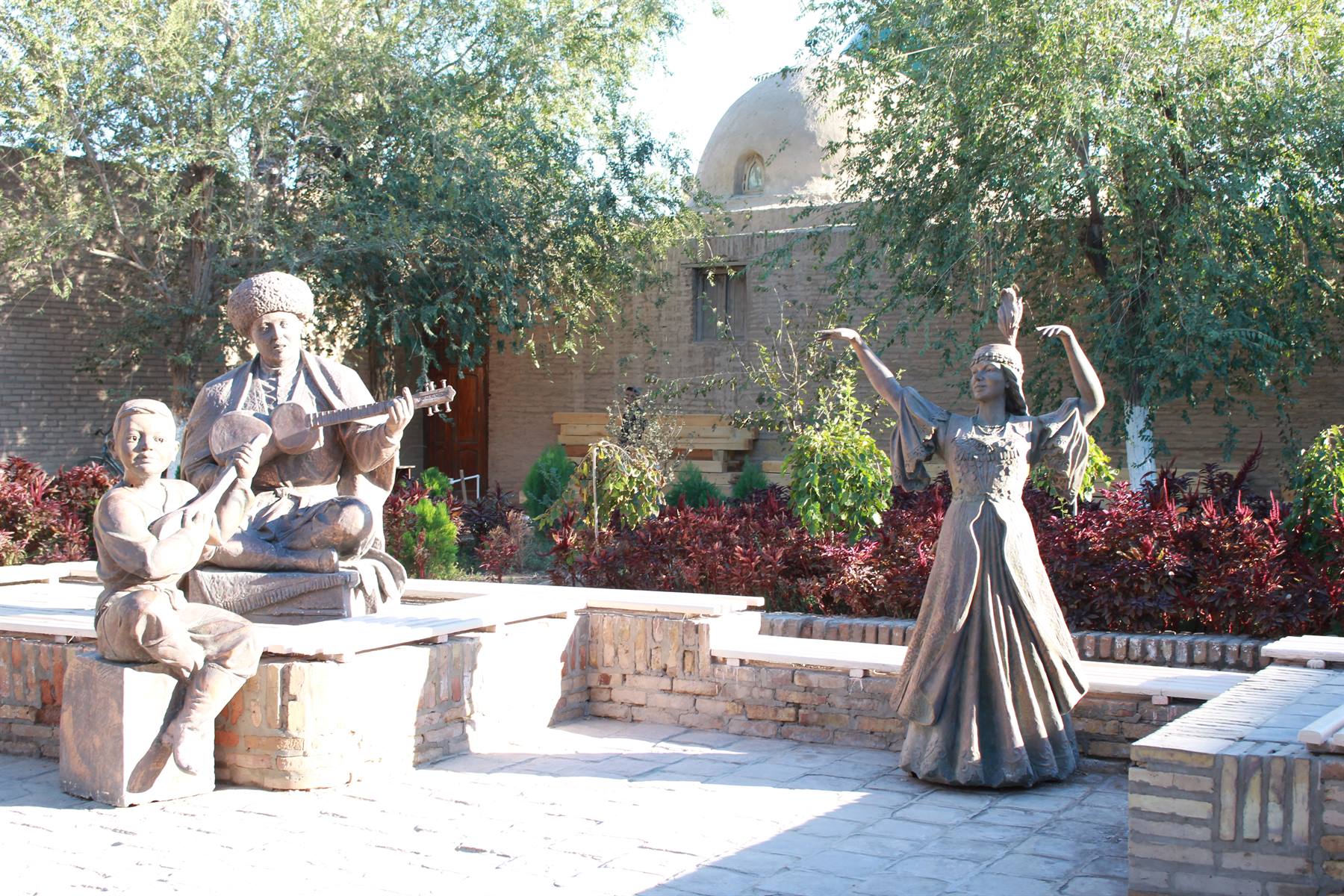 Statue di bronzo di musicisti e ballerina tra mattoni e alberi a Khiva