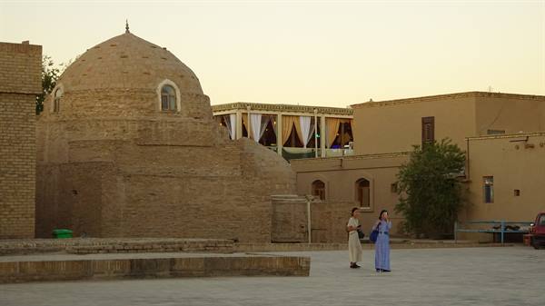 Due donne passeggiano davanti a un mausoleo in mattoni di Khiva