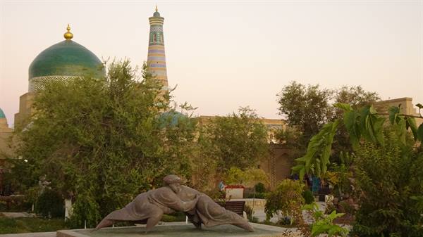 Khiva: statua di lottatori davanti al minoreto Islam Khoja al crepuscolo