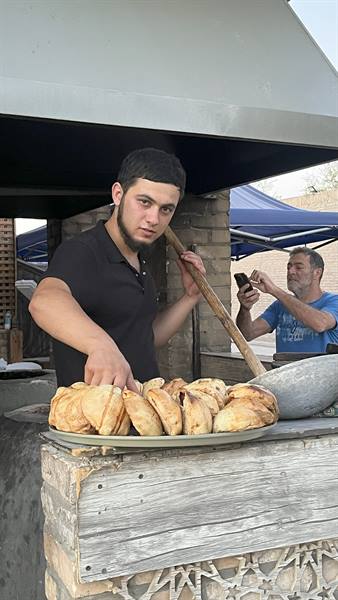 Giovane fornaio con vassoio di samsa davanti al forno a Samarcanda