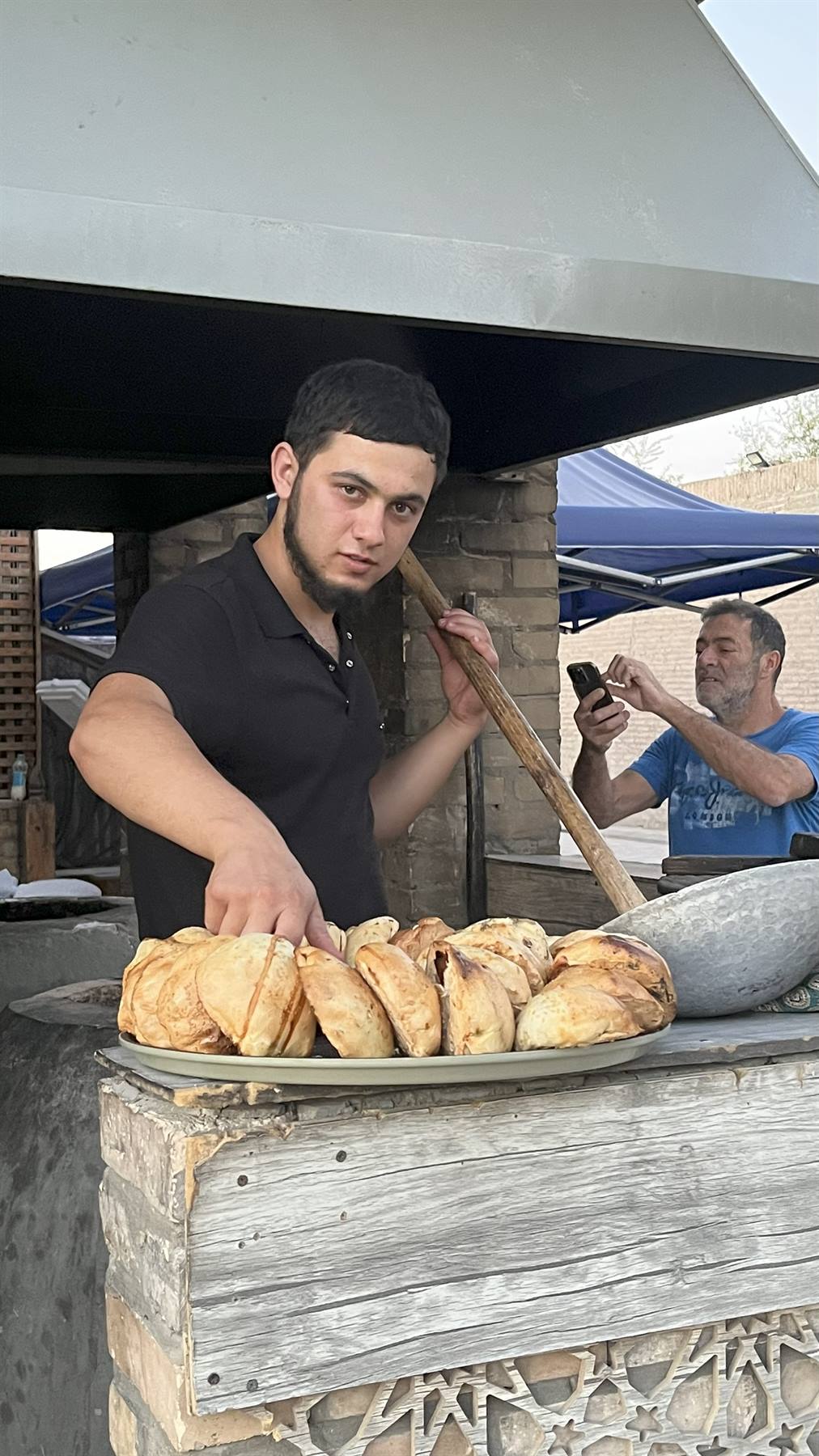 Giovane fornaio con vassoio di samsa davanti al forno a Samarcanda