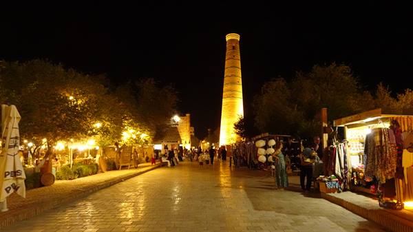 Il minareto illuminato di notte sopra il viale dei banchi di Khiva