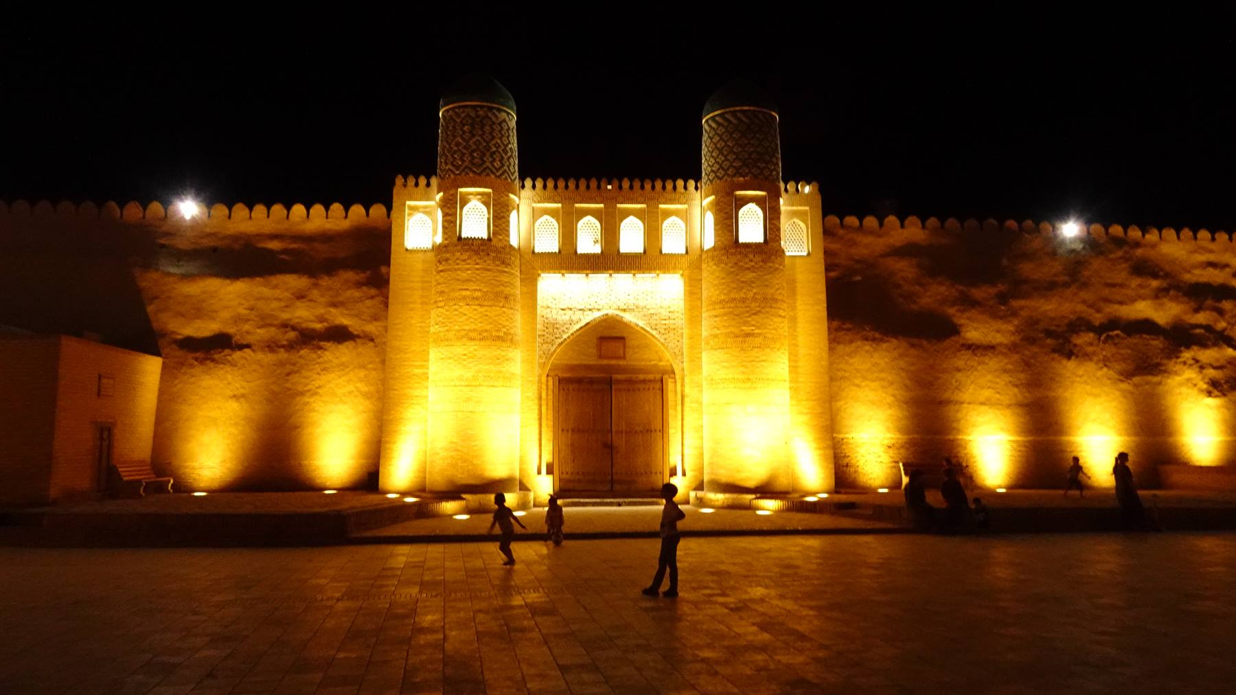 Mura illuminate di notte a Khiva, bambini che corrono nella piazza