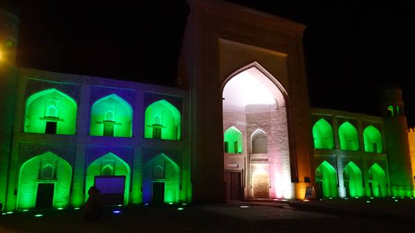 Madrasa di mattoni illuminata di verde e rosa di notte a Bukhara