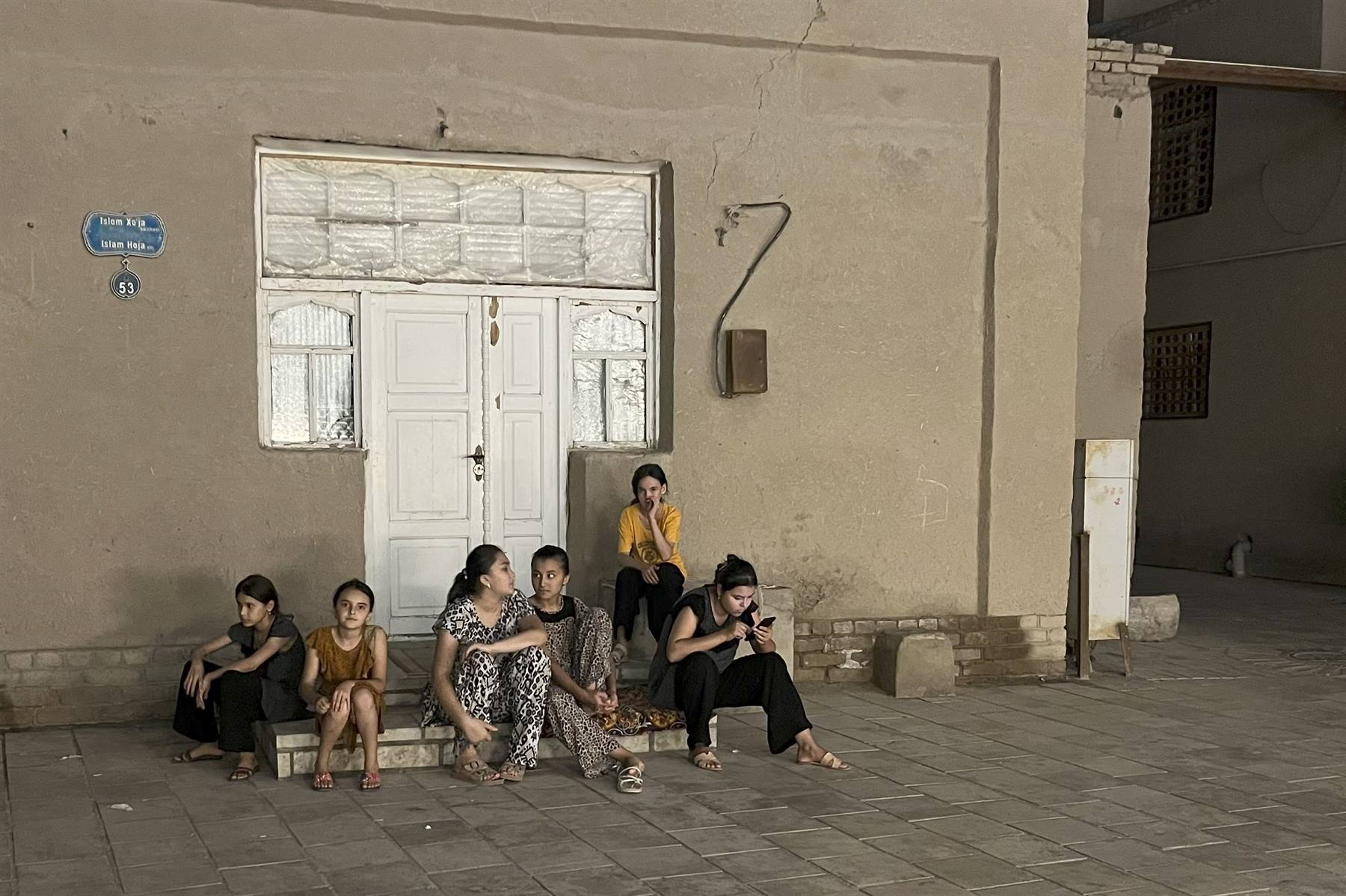 Ragazze sedute davanti a una porta bianca di Bukhara al crepuscolo