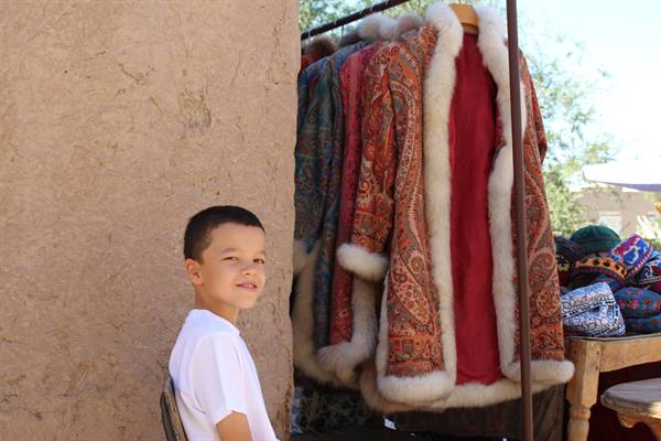 Bambino sorridente accanto a pellicce e cappotti tradizionali in vendita a Khiva