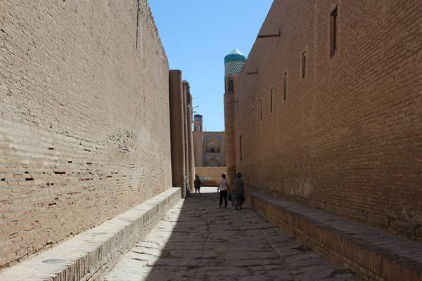 Turisti camminano nel vicolo tra muri di mattoni, a Khiva