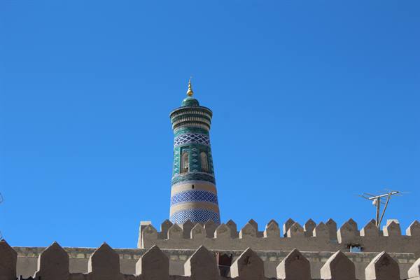 Il minareto maiolicato verde e azzurro svetta oltre le mura merlate di Khiva
