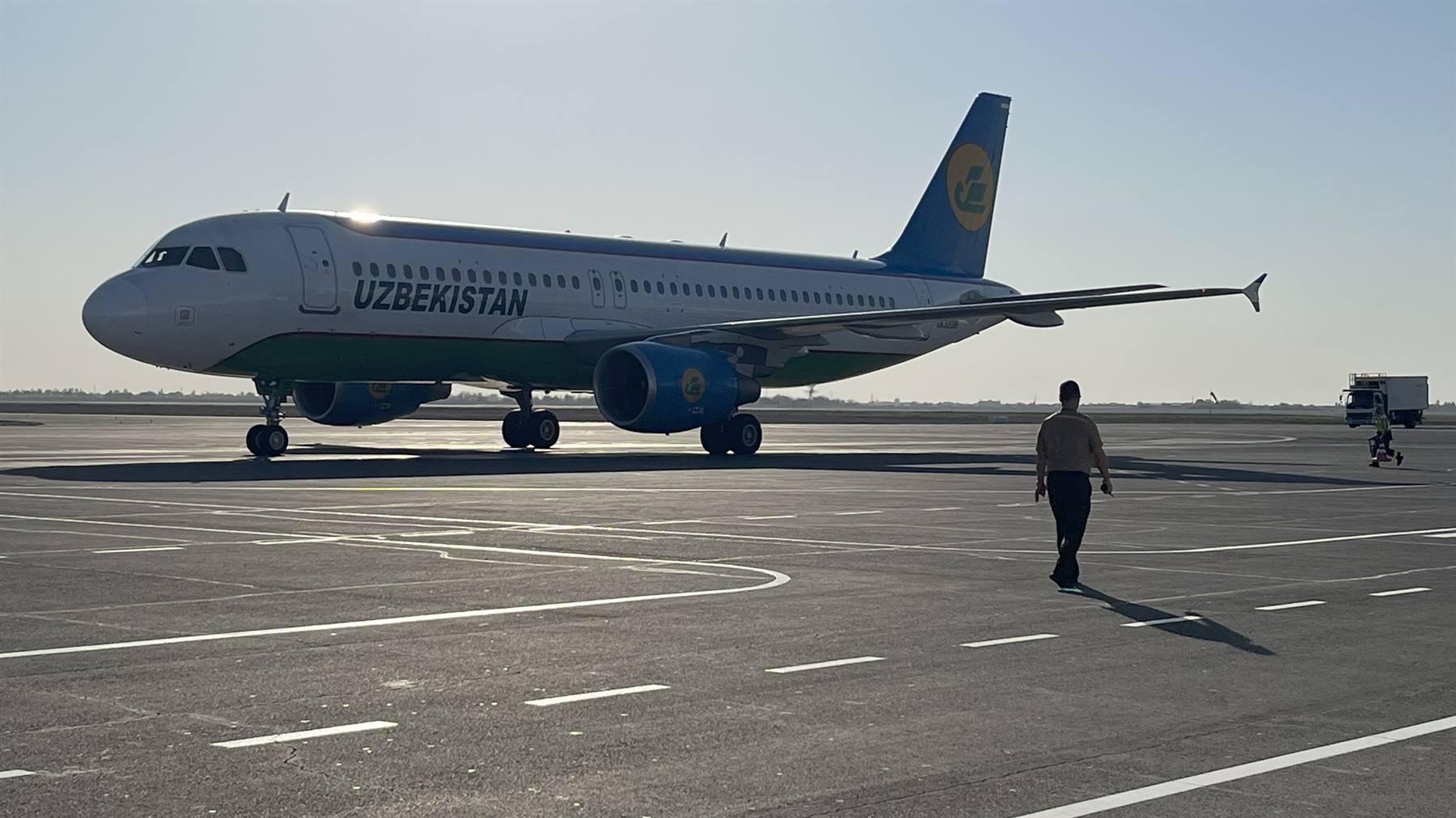 Aereo Uzbekistan Airlines sul piazzale, uomo cammina sotto il sole