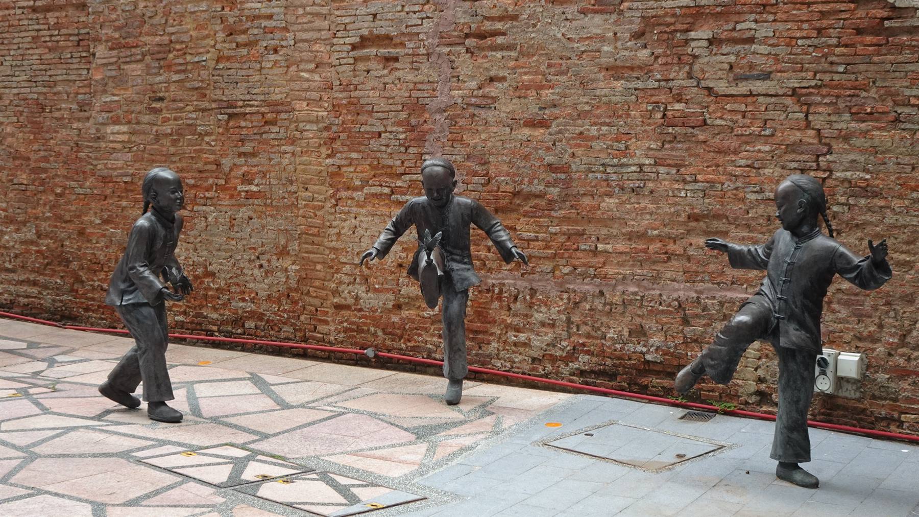 Statue in bronzo di bambini che giocano contro un muro di mattoni rossi