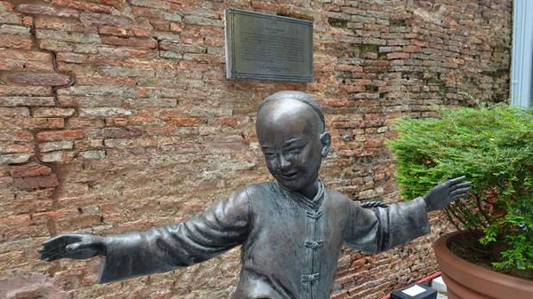 A bronze child dances happily among ancient bricks and greenery.