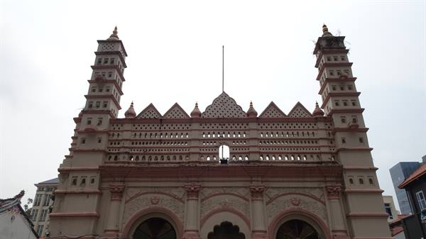 Pink facade of Nagore Dargah mosque with two pierced minarets, grey sky