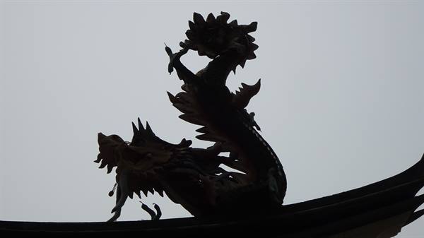 Dragon statue silhouetted on a curved temple roof against gray sky