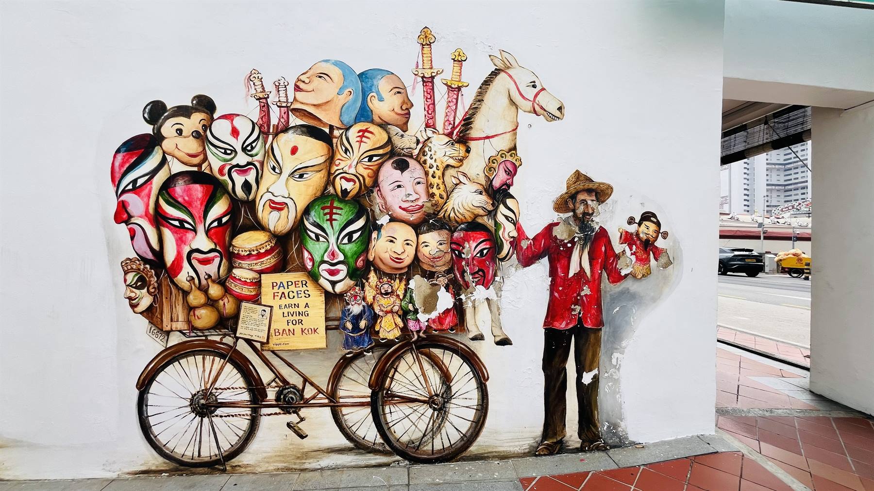 Murale: venditore in cappello accanto a bicicletta carica di maschere dipinte e cavalli