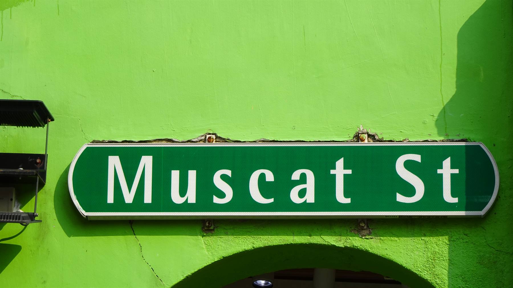 Insegna verde con scritta bianca Muscat St su muro verde acceso