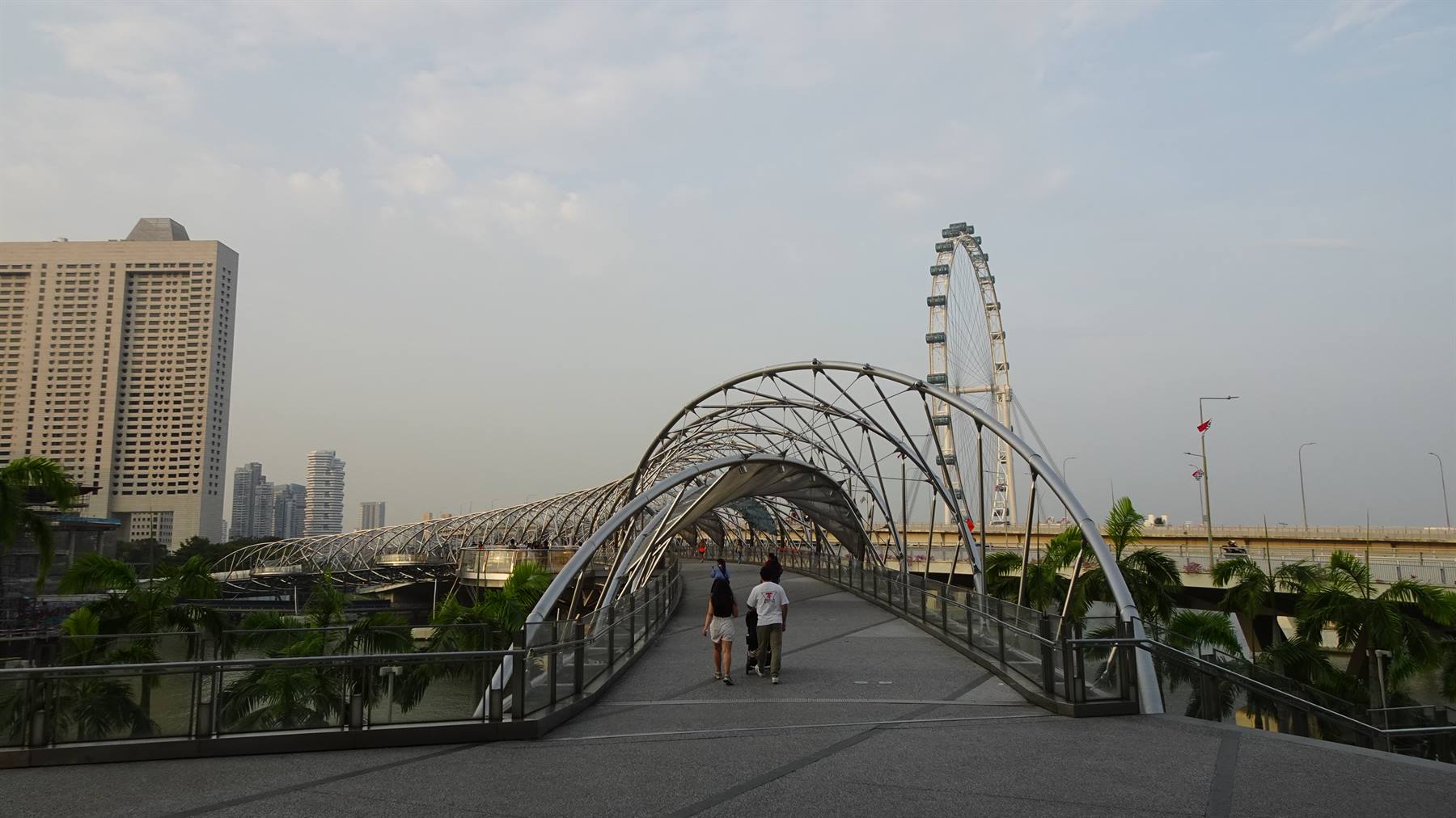 Passeggeri camminano sulla Helix Bridge d'acciaio, con la ruota Singapore Flyer sullo sfondo