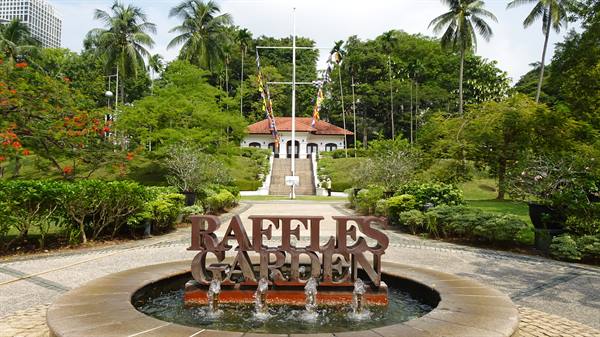 Fountain with wooden sign in front of white pavilion with red roof, palms