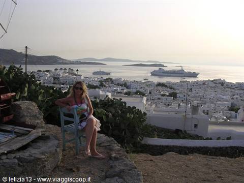 Tourist on a light-blue chair above Mykonos, white houses and cruise ship