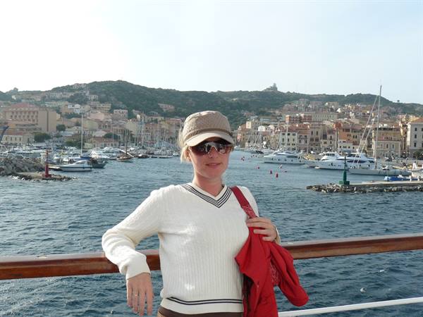 Woman in cap and white sweater by La Maddalena harbor among yachts and colorful houses