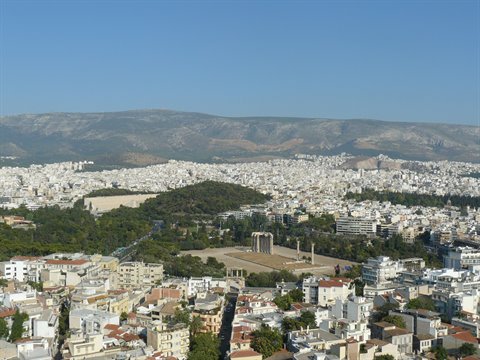 Athens: white buildings, ancient columns and green hill under dry mountains