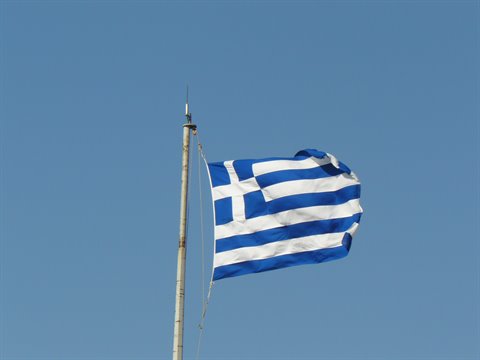 Greek flag with blue and white stripes waving on a pole against clear blue sky
