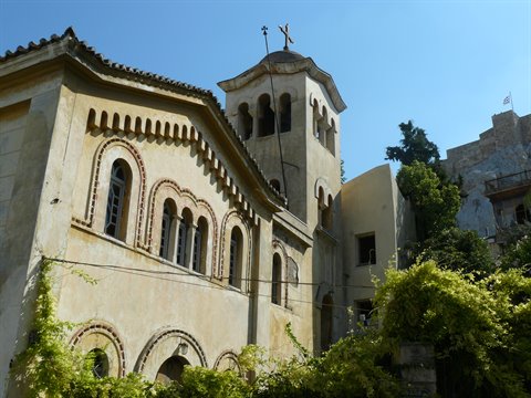 Byzantine stone church with bell tower and arched windows, green vines, blue sky