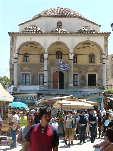 Tzistarakis Mosque in Athens, tiled domes, Greek flag, crowd under market umbrellas