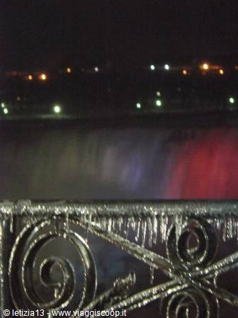 Ice-covered iron railing in front of the illuminated falls at night