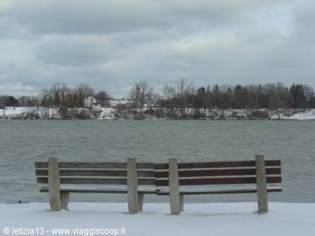 Two wooden snow-dusted benches facing a cold wintry river shore