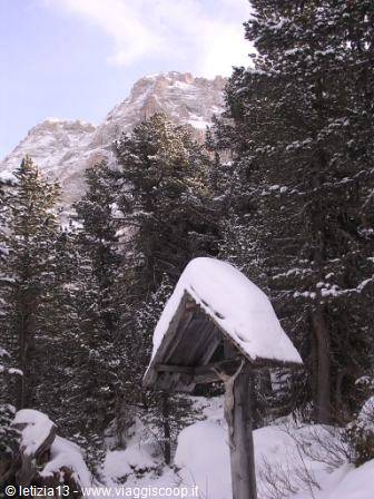Snow-covered wooden shrine among fir trees, Dolomite cliff behind